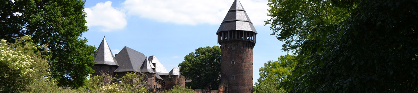 Burg Linn in Krefeld umgeben von Bäumen im Sommer